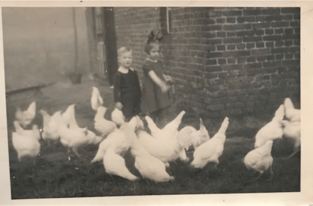 meisje en jongetje bij kippen voor huis op zwartwitfoto